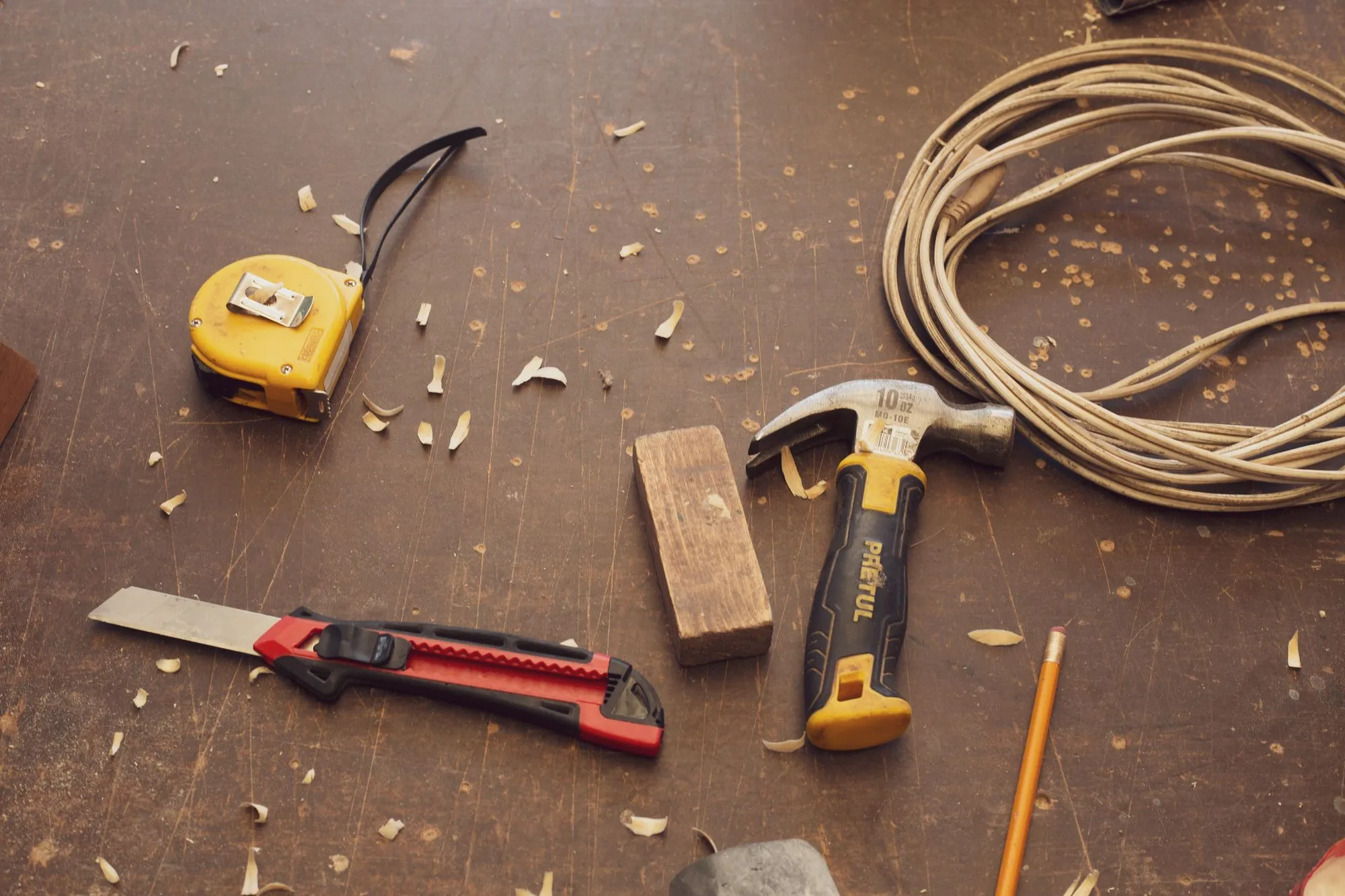 A tape measure, hammer and pencil laid out on a workbench