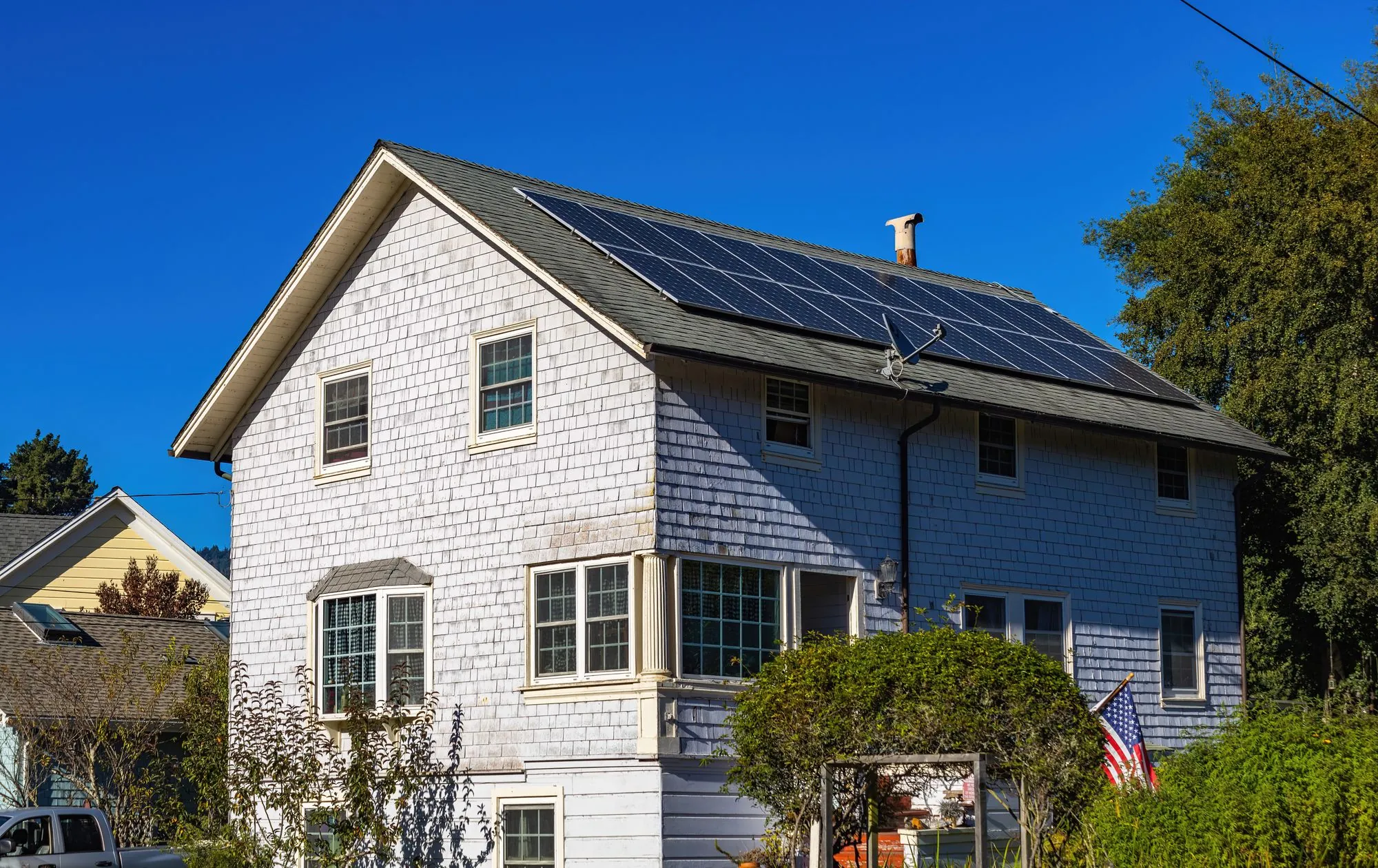 A shingled two-storey house with dormer windows on a clear day
