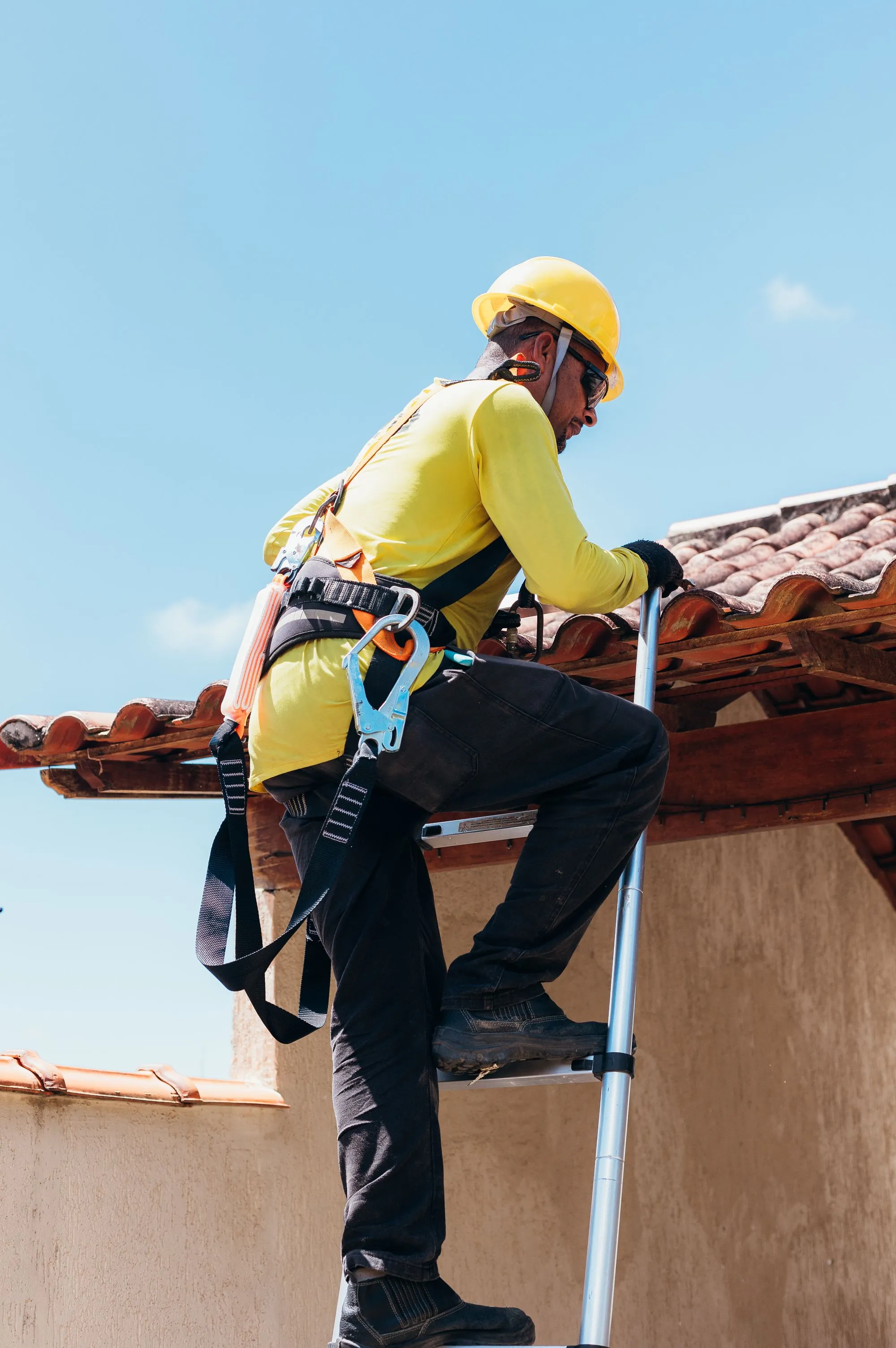 A harnessed roofer kneeling on a roof to inspect it
