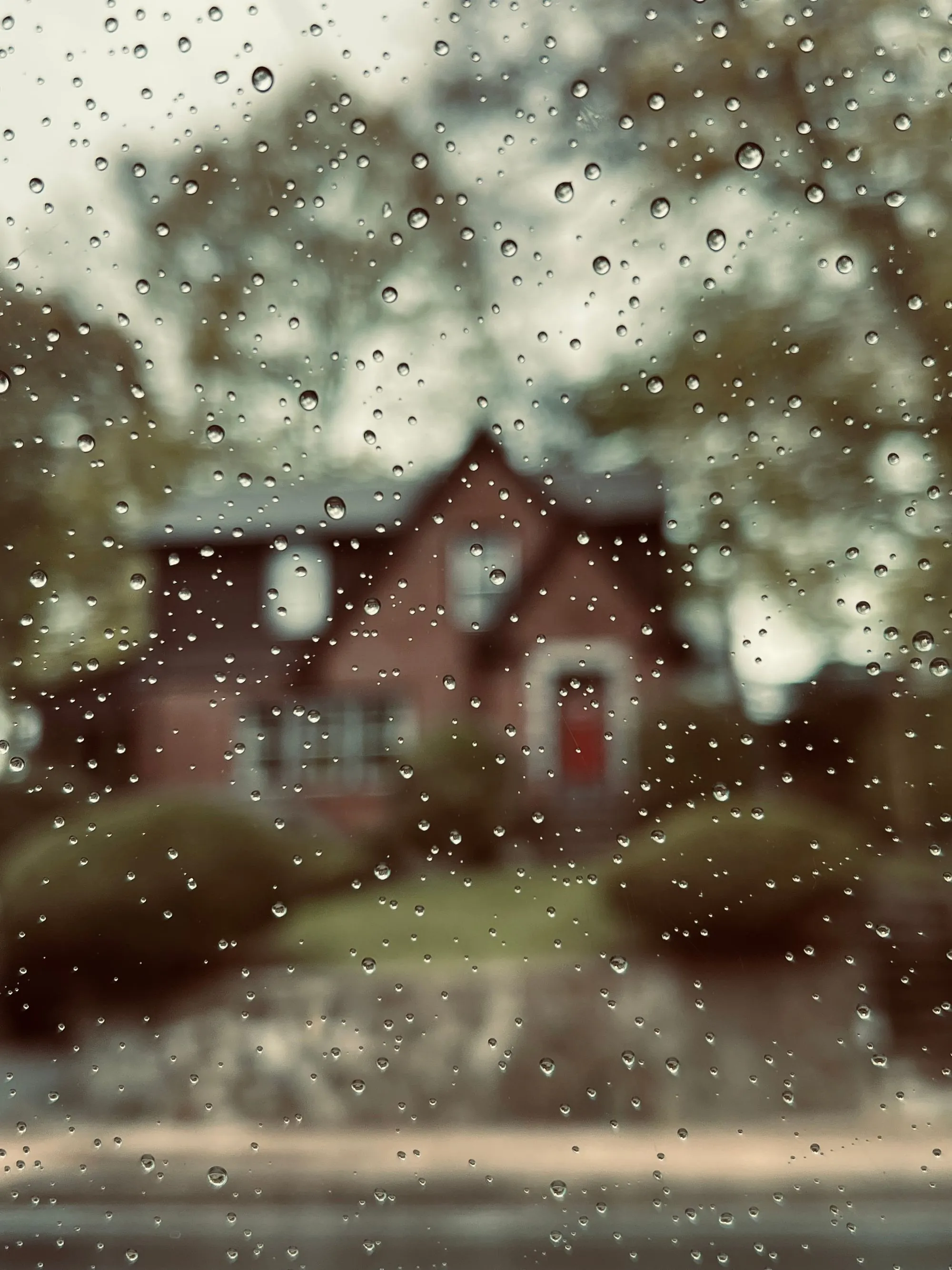 Heavy rain running down a window with a house behind it